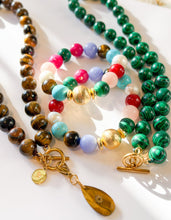Load image into Gallery viewer, A set of colorful beaded jewelry bracelets and necklaces arranged on a white surface. The collection includes a green malachite bead necklace, a brown tiger's eye bead necklace with gold toggle clasp and teardrop charm, a multi-colored bead bracelet with gold and green beads, and a pastel bead bracelet.