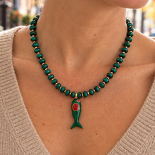 Load image into Gallery viewer, A close-up lifestyle shot of a woman wearing a green beaded necklace with a green fish-shaped pendant featuring a red eye, styled with a beige knit sweater.
