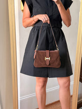 Load image into Gallery viewer, A woman takes a mirror selfie showing a black dress with a pleated skirt and a brown suede shoulder bag with a gold clasp. She is wearing beige pointed-toe heels in an indoor setting with a wooden floor and a mirror frame visible.
